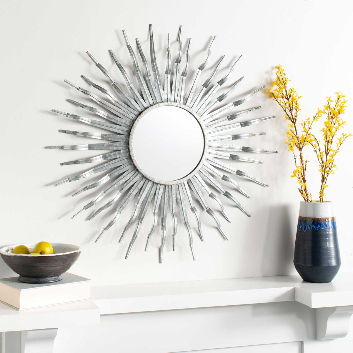 Silver sunburst mirror brings an airy metallic accent to a wall above a white mantel