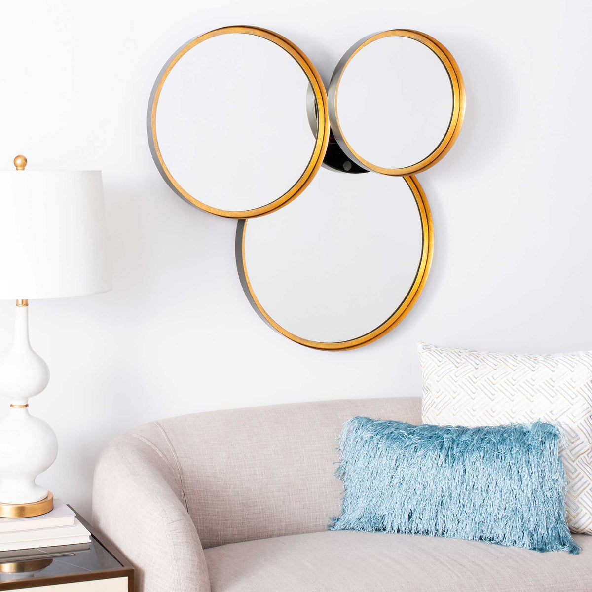 Overlapping round mirrors with warm gold borders create a sculptural accent above a sofa.