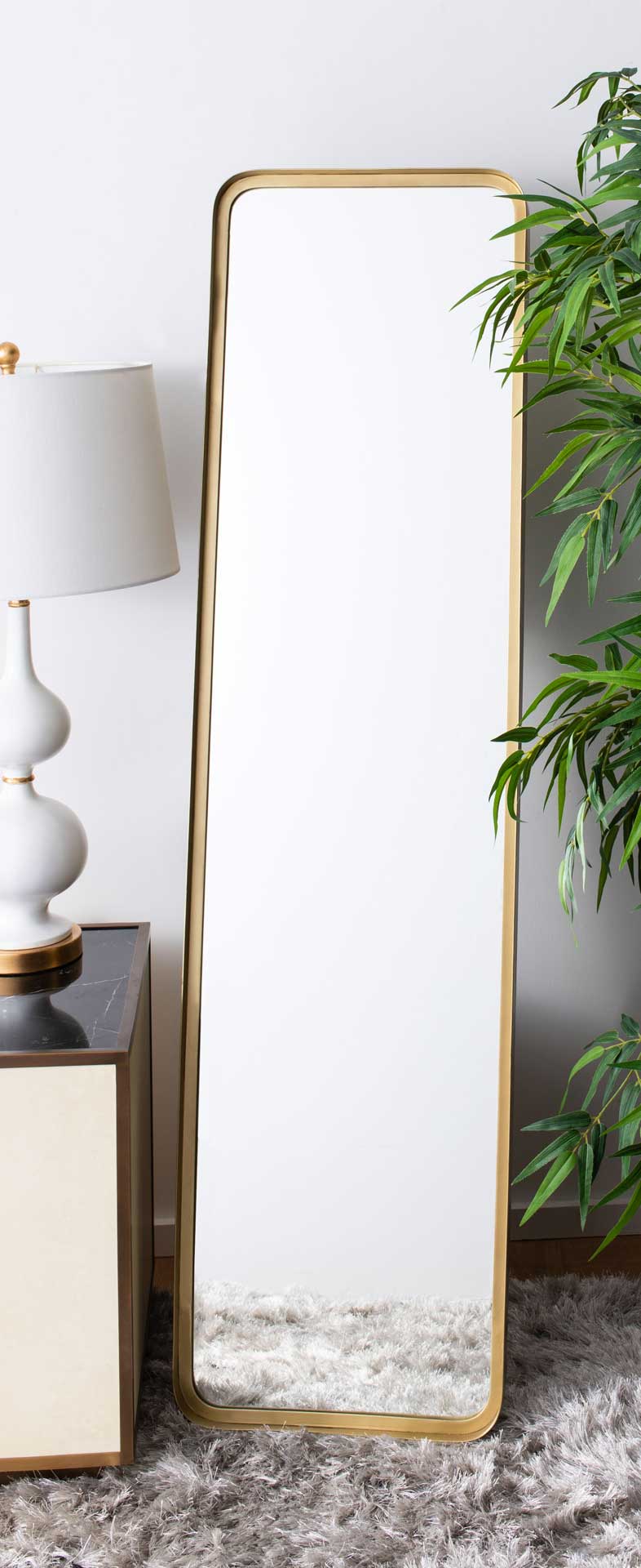 Full-length brass-tone mirror adds warmth beside neutral furnishings and greenery
