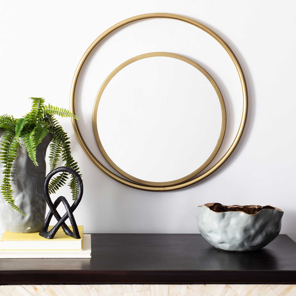 An airy brass-finished mirror adds a warm, sculptural accent above a dark console