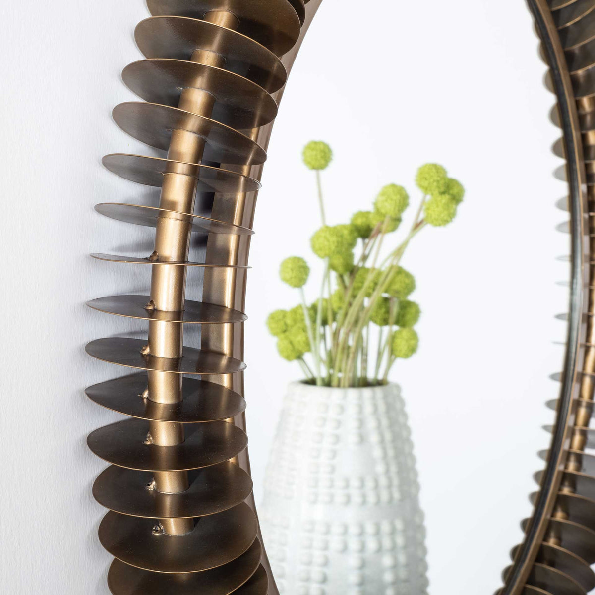 Slim metal discs flare from a curved antique brass rail, creating a richly textured frame.