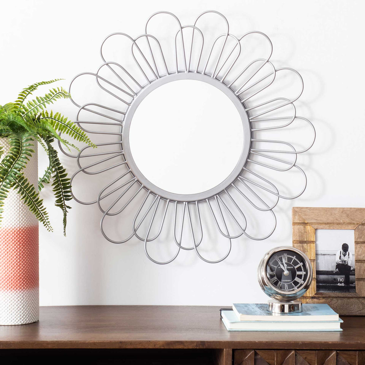 Delicate silver wire petals frame a round wall mirror above a wood console