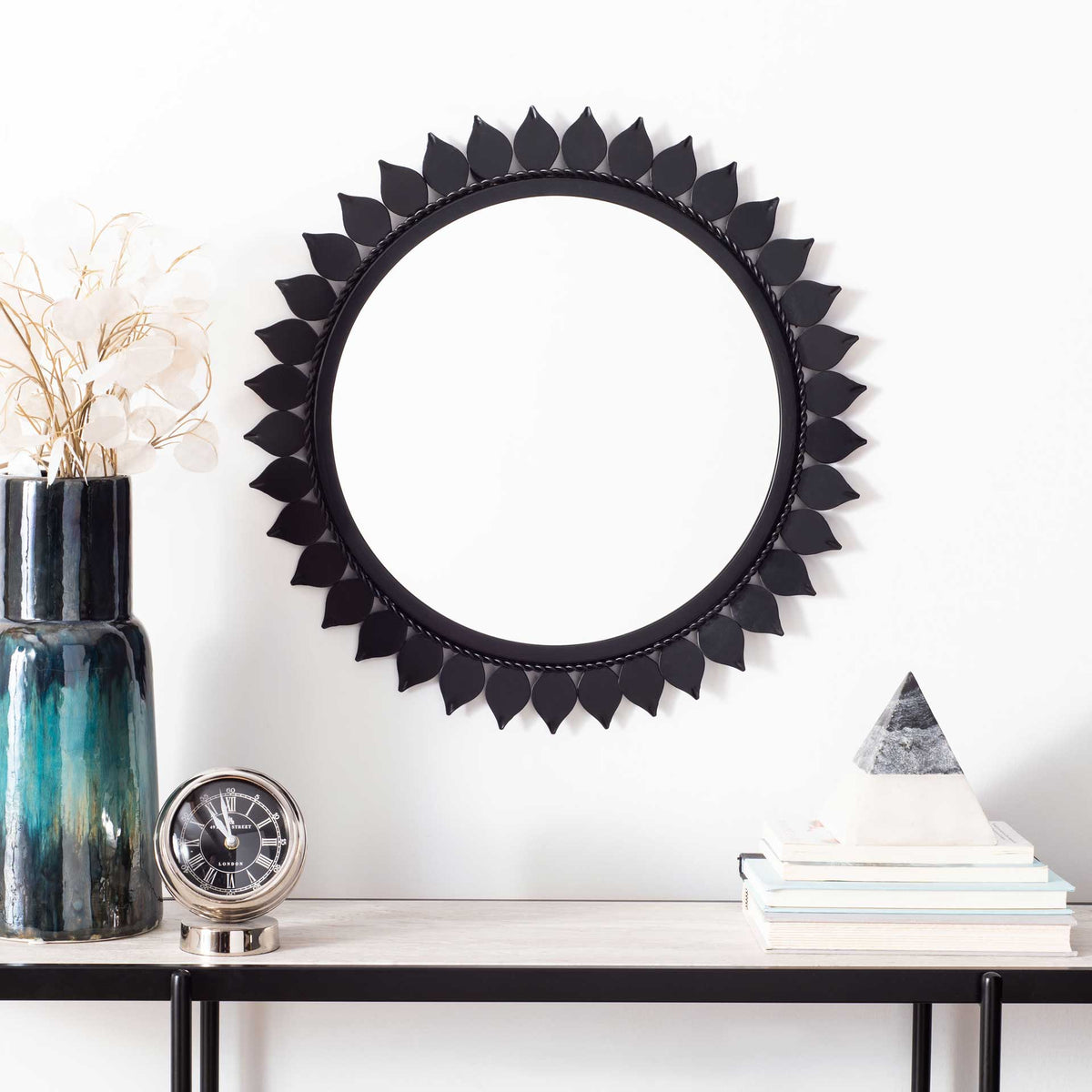 Sculptural leaf accents bring striking texture to this round black wall mirror