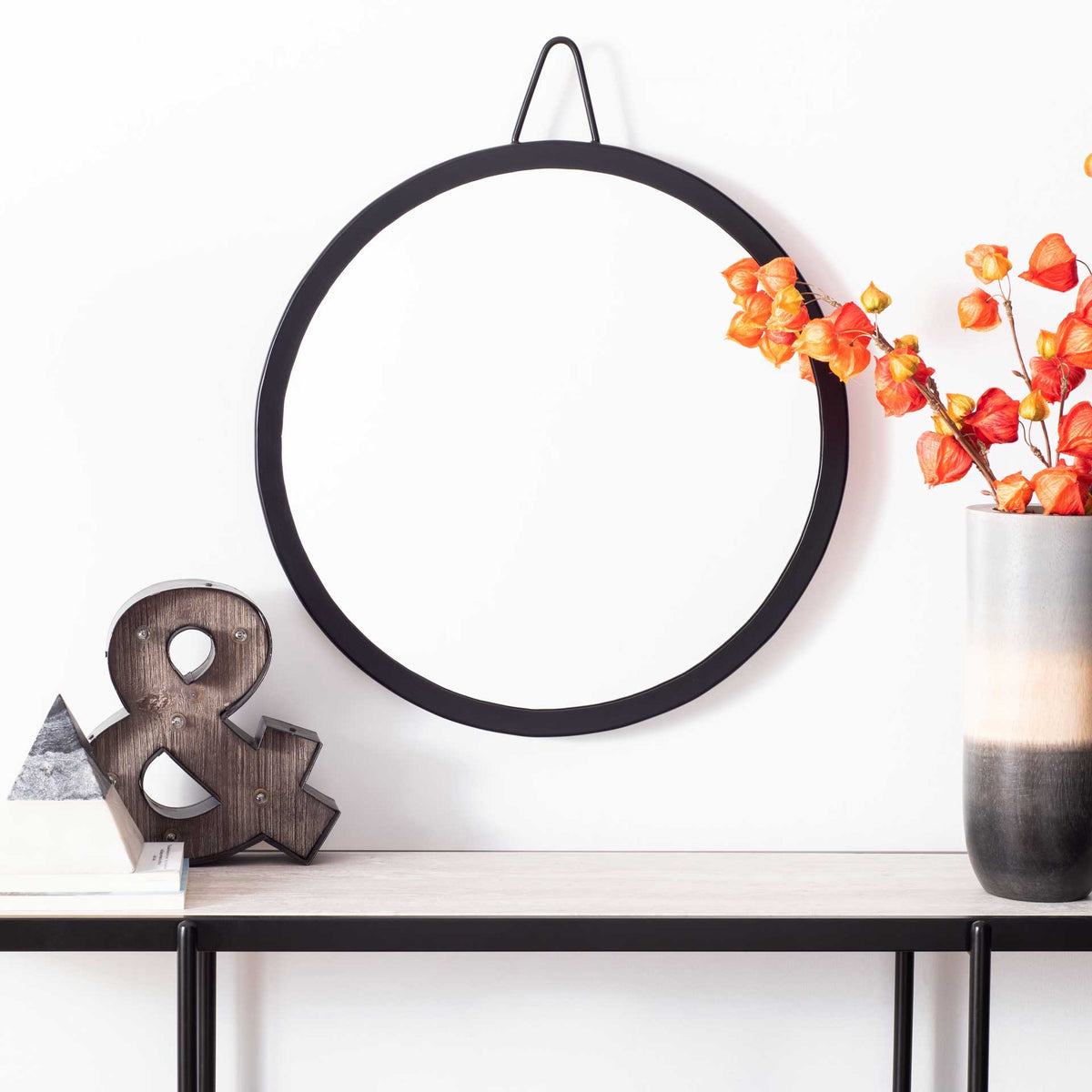 A round black-framed mirror adds a minimalist accent above a console table.