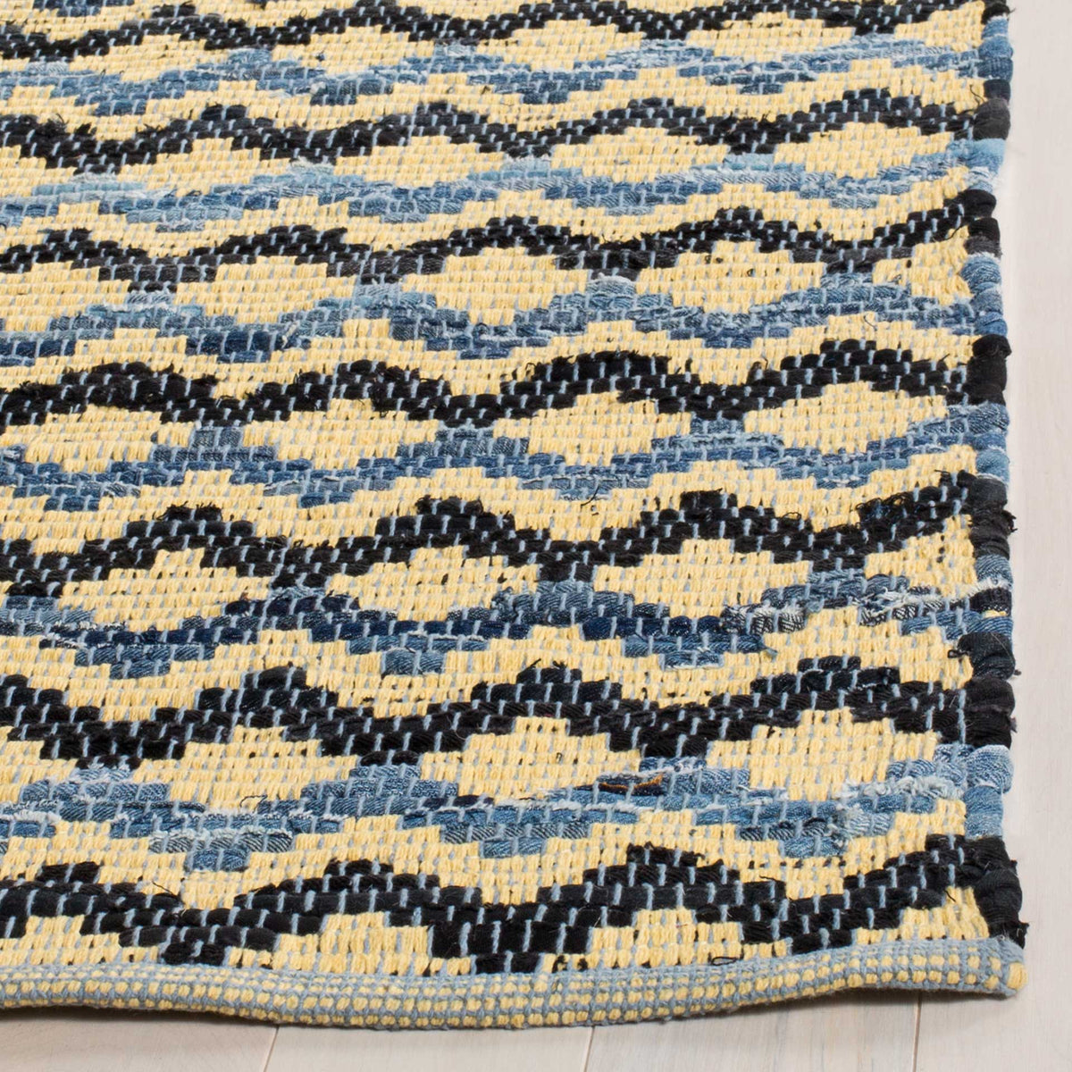 Gold, blue, and black cotton yarns form undulating motifs beside the finished rug edges