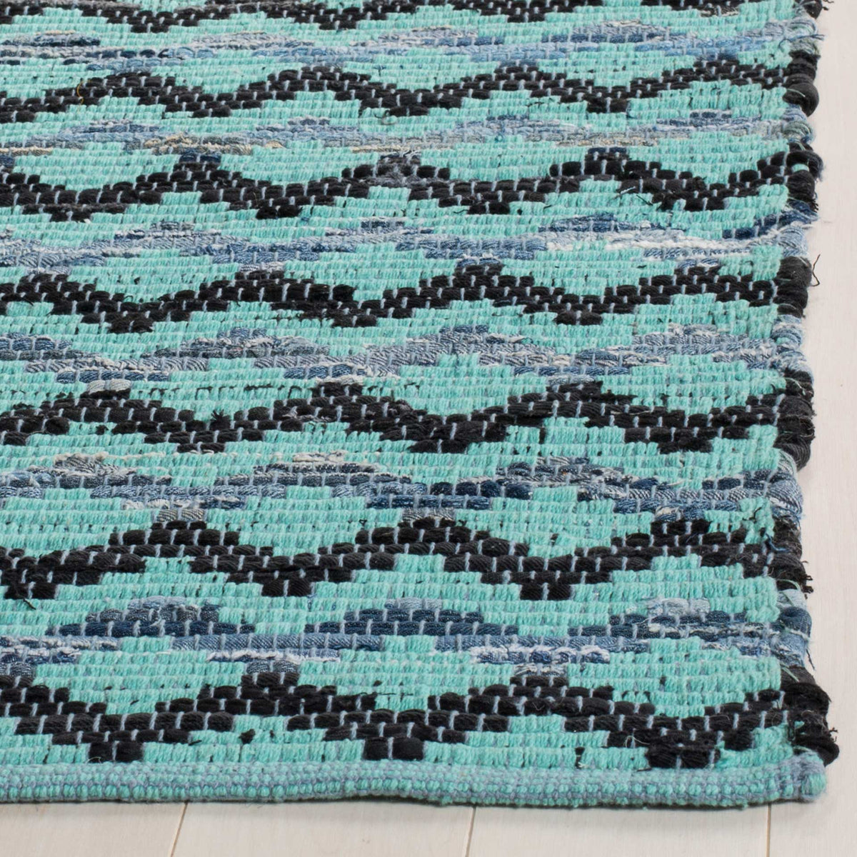 Turquoise cotton yarns form raised black wave stripes beside the finished rug corner