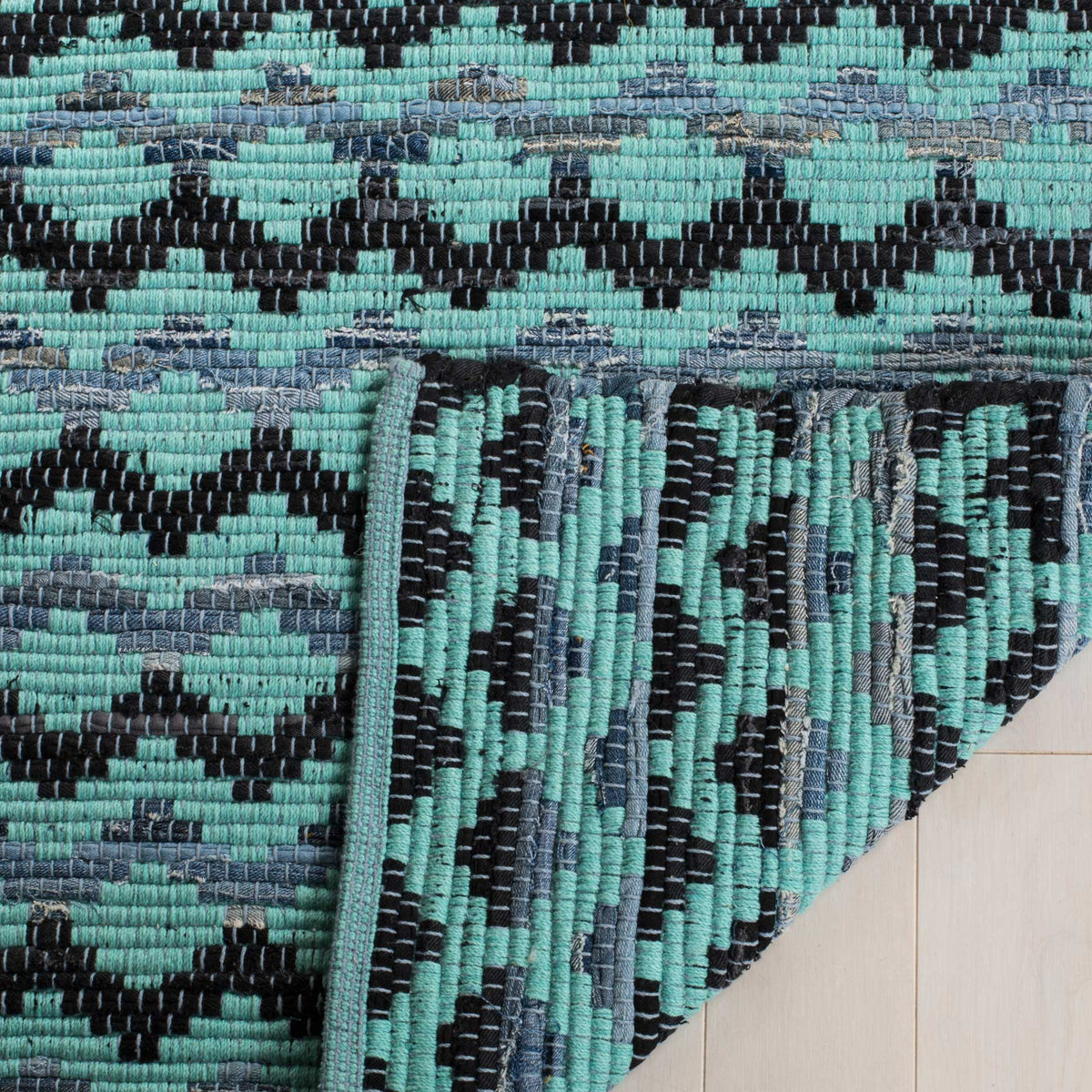 Folded turquoise rug corner reveals black and blue yarns woven through its underside