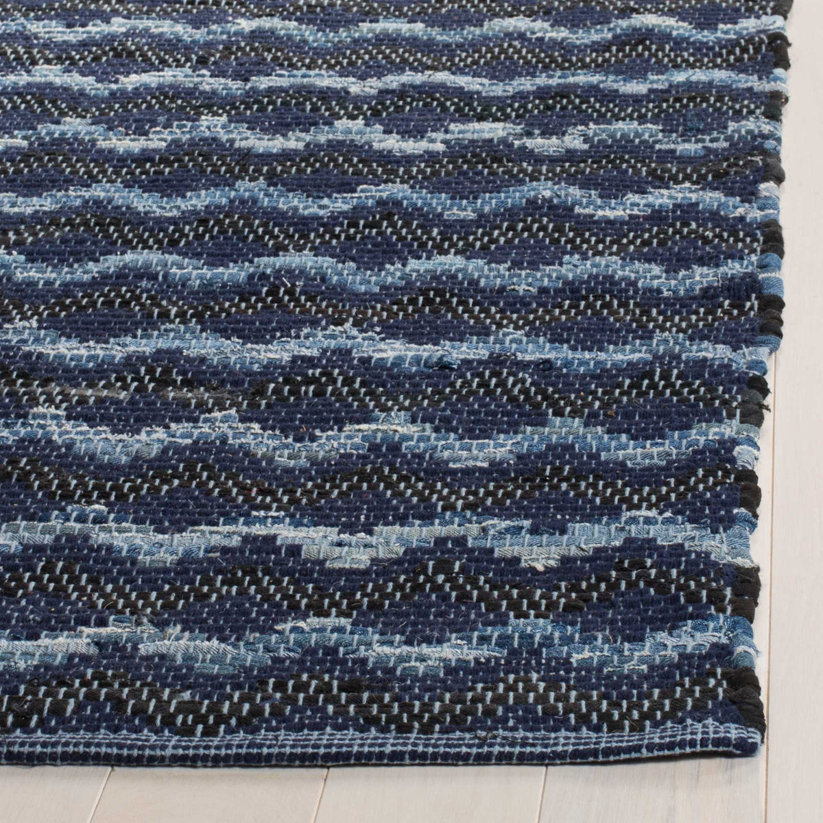 Finished rug corner reveals navy, black, and soft blue waves in the textured cotton weave