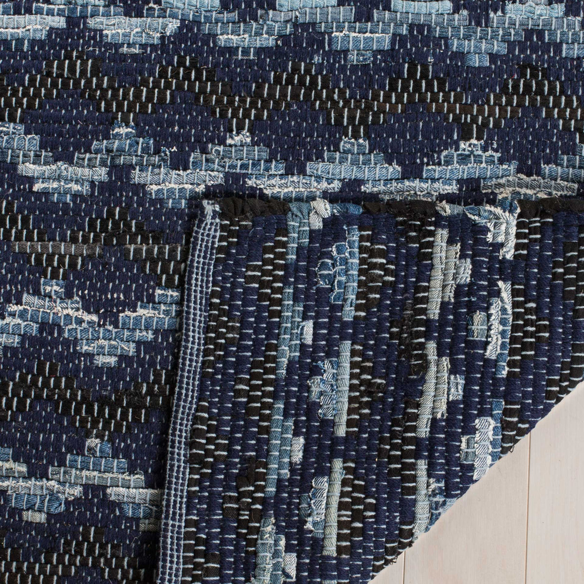 Folded cotton rug corner reveals its navy, black, and light blue woven underside