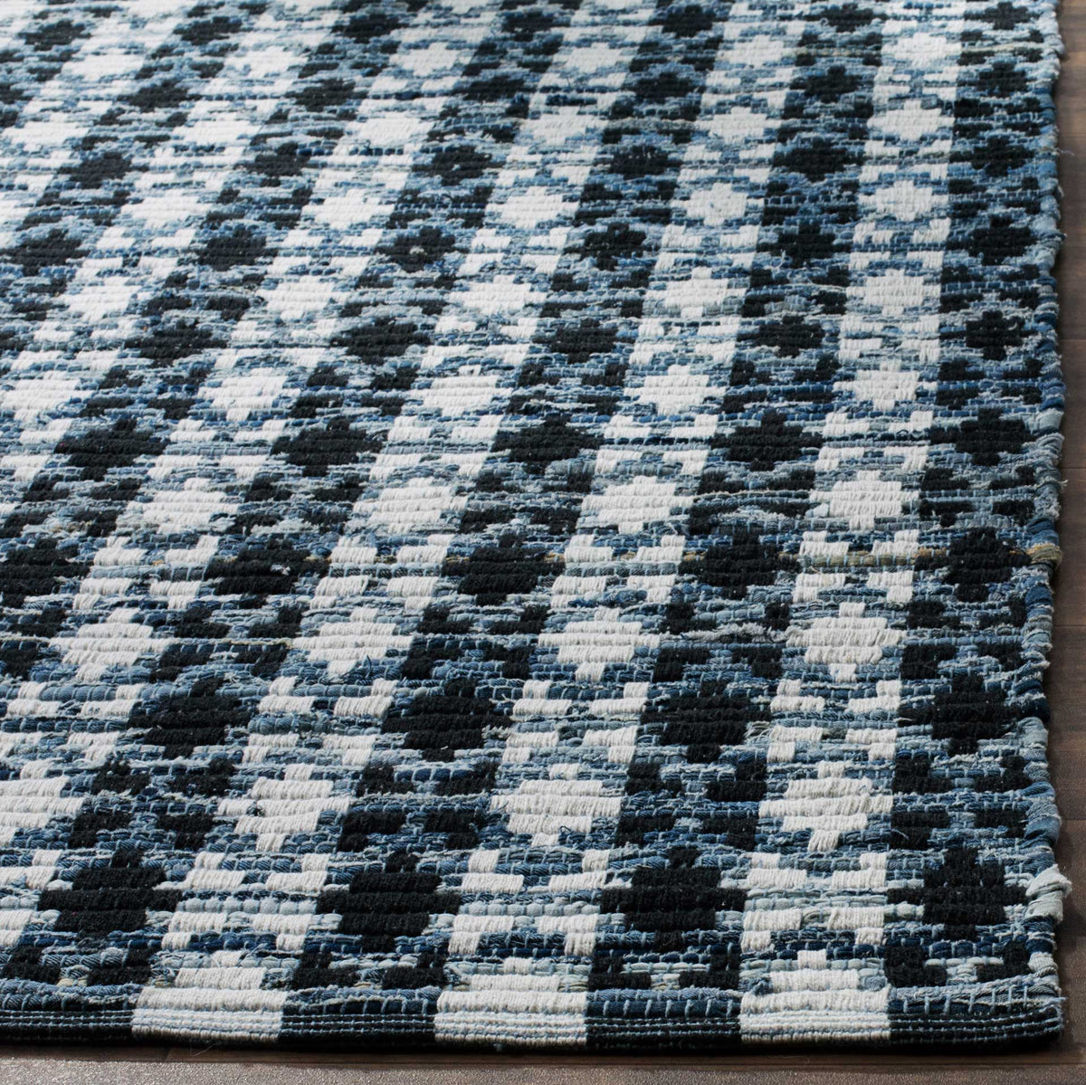 Textured black and ivory yarns meet the neatly finished edge of this blue cotton rug