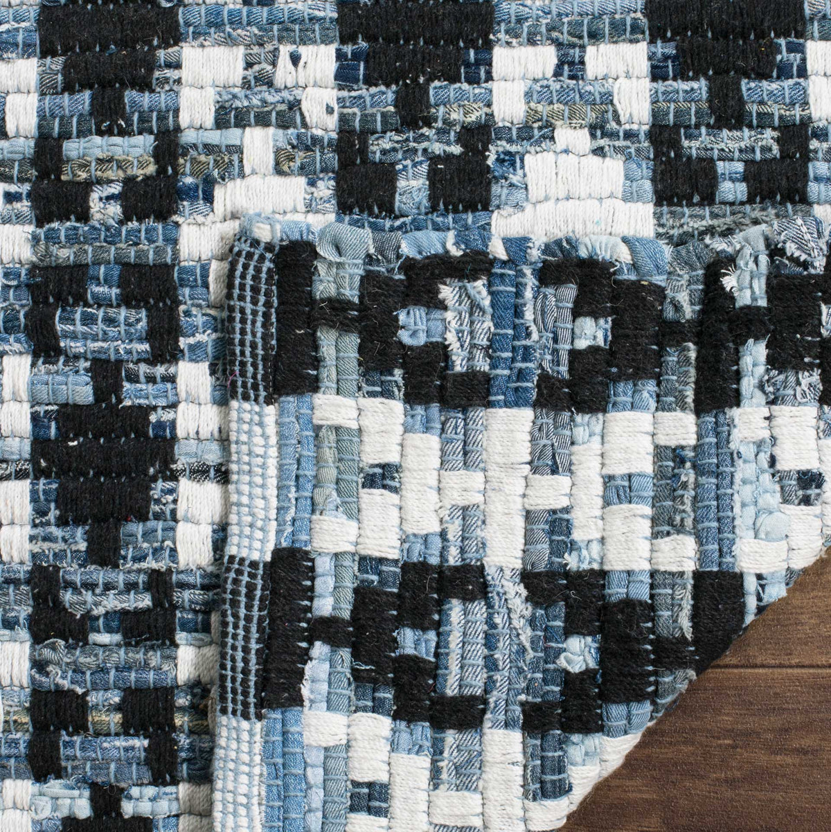 A folded corner exposes the black, ivory, and blue cotton weave on the rug's underside