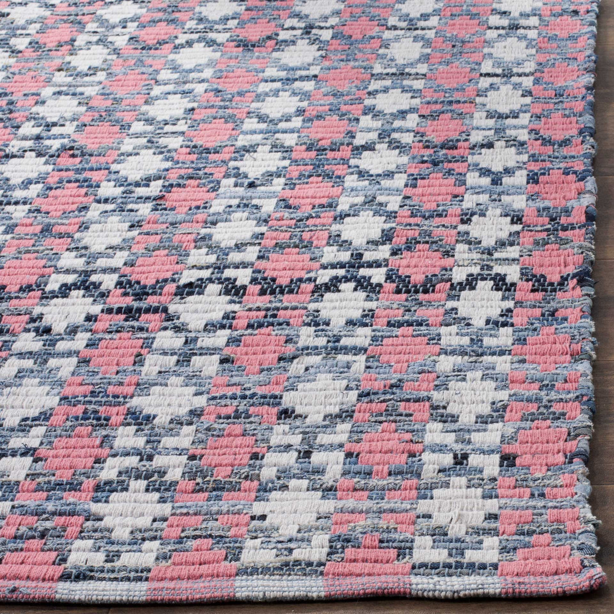 Coral and navy cotton threads form tactile motifs along the rug's neatly finished edge