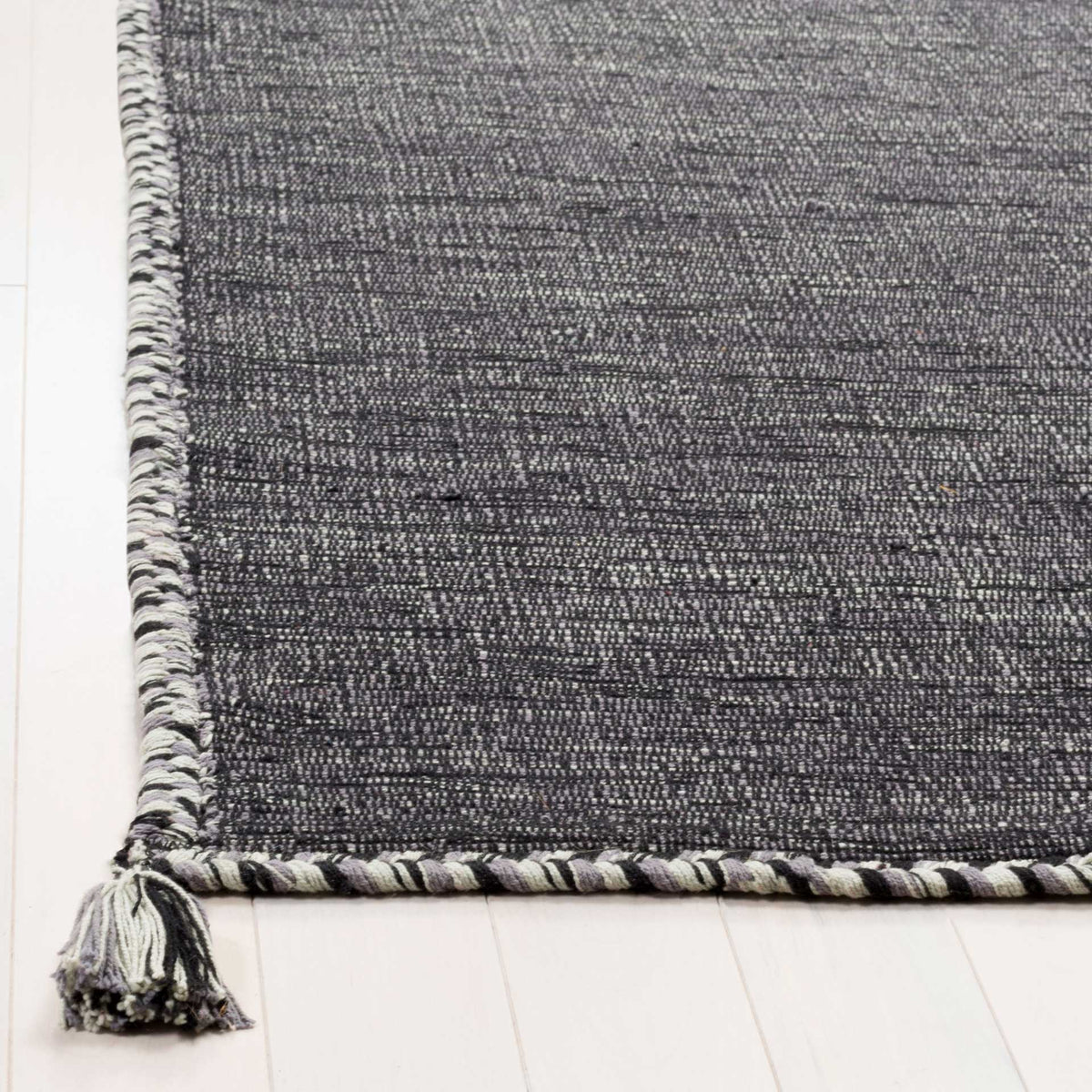 Gray and black braided trim and a soft corner tassel finish the textured cotton rug.
