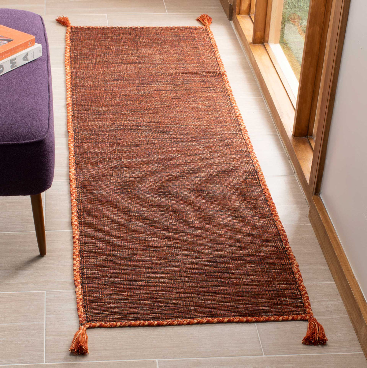 Warm orange threads stand out against black in this slim textured runner with corded edges and tassels