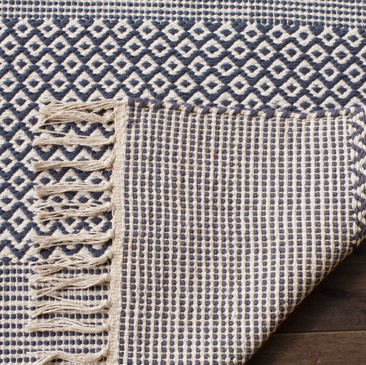 Folded navy and ivory cotton rug reveals a finely striped backing and fringed edge