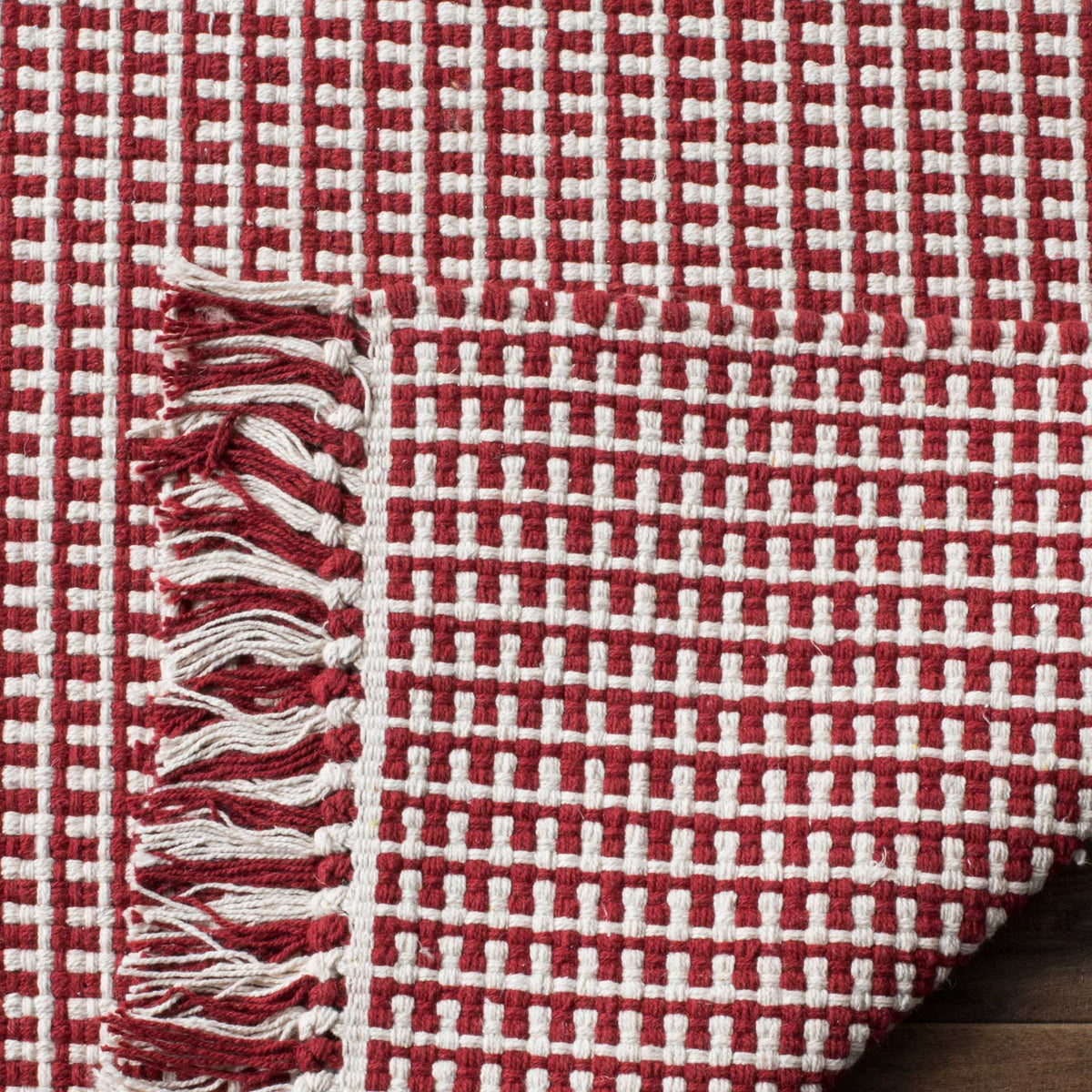 Red and ivory cotton rug has a densely woven underside and loose fringe