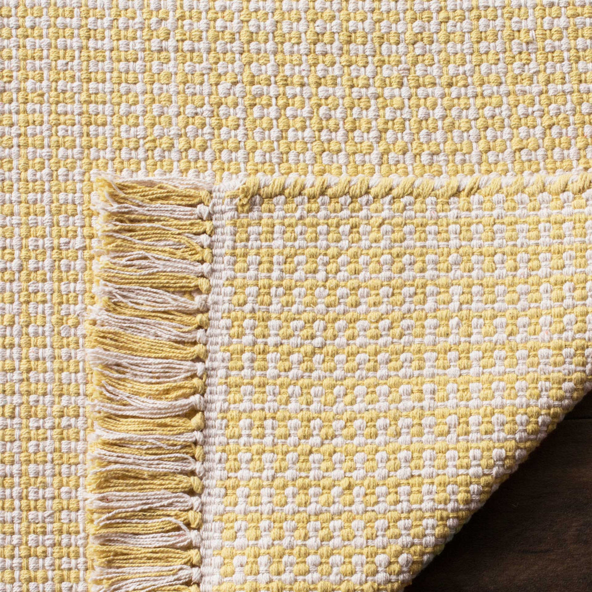 Ivory and yellow cotton rug has a dense woven underside and two-tone fringe