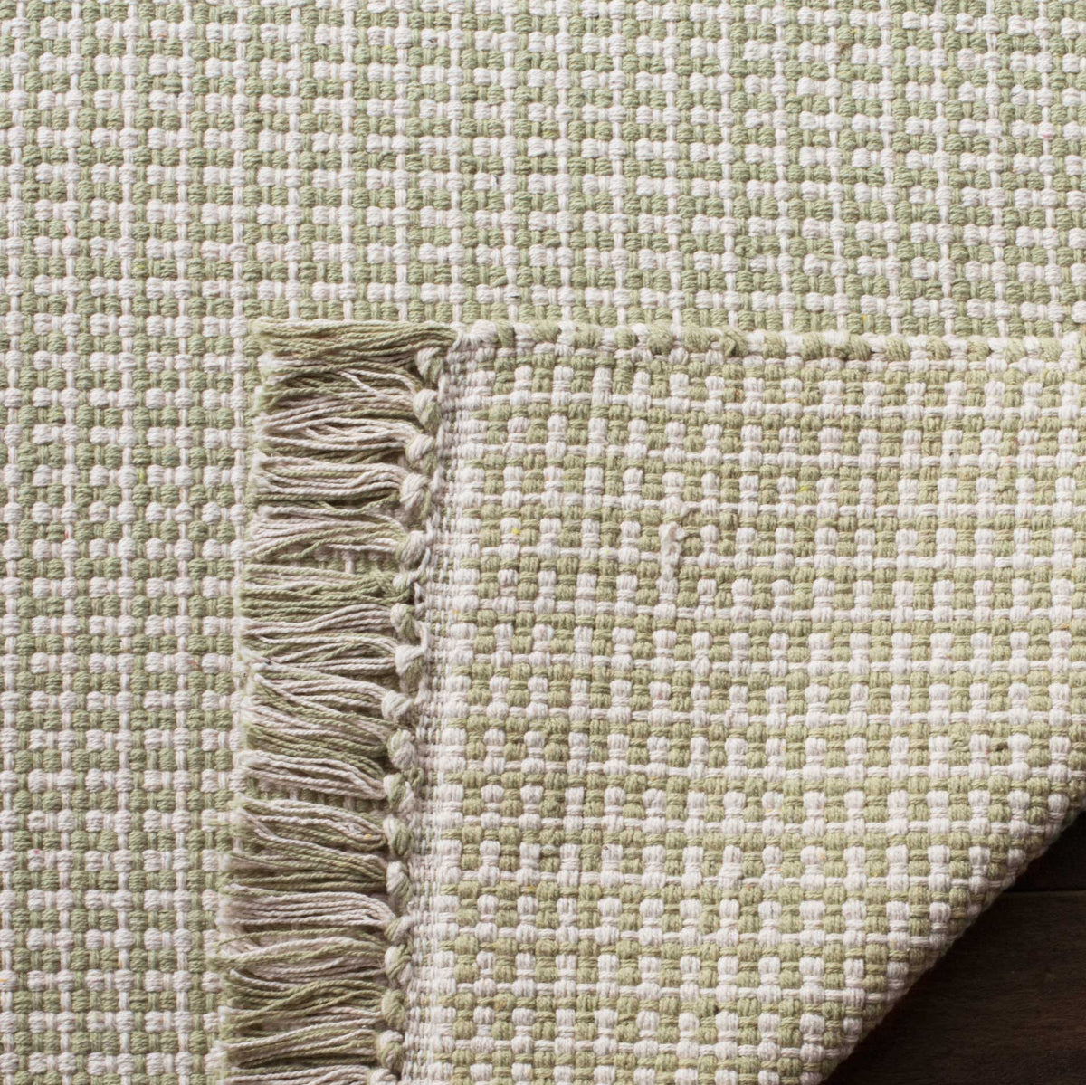 Ivory and green cotton rug has a tightly woven underside and mixed-color fringe
