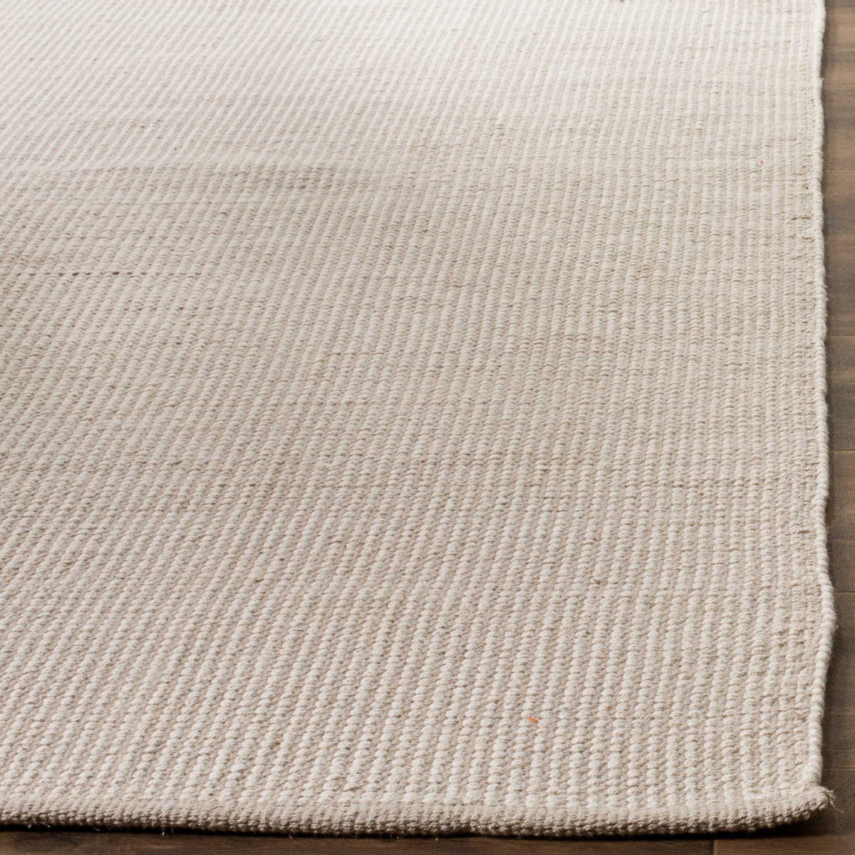 Softly raised cotton rows bring subtle ivory and gray texture to the rug's bound corner.