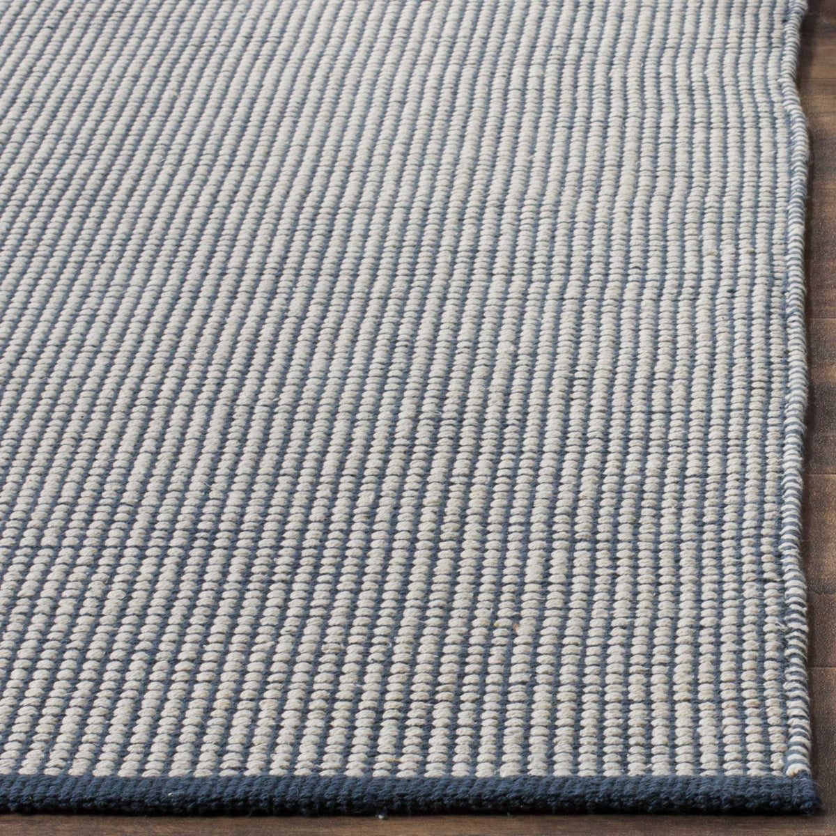 A neatly bound navy border finishes the rug's rows of raised ivory cotton loops.