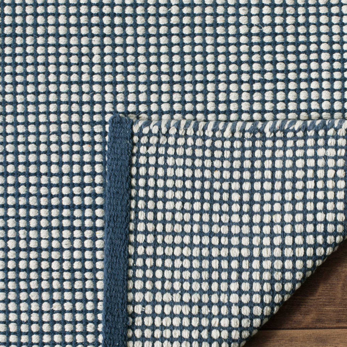 Tiny ivory checks carry through to the rug's underside and folded navy border.
