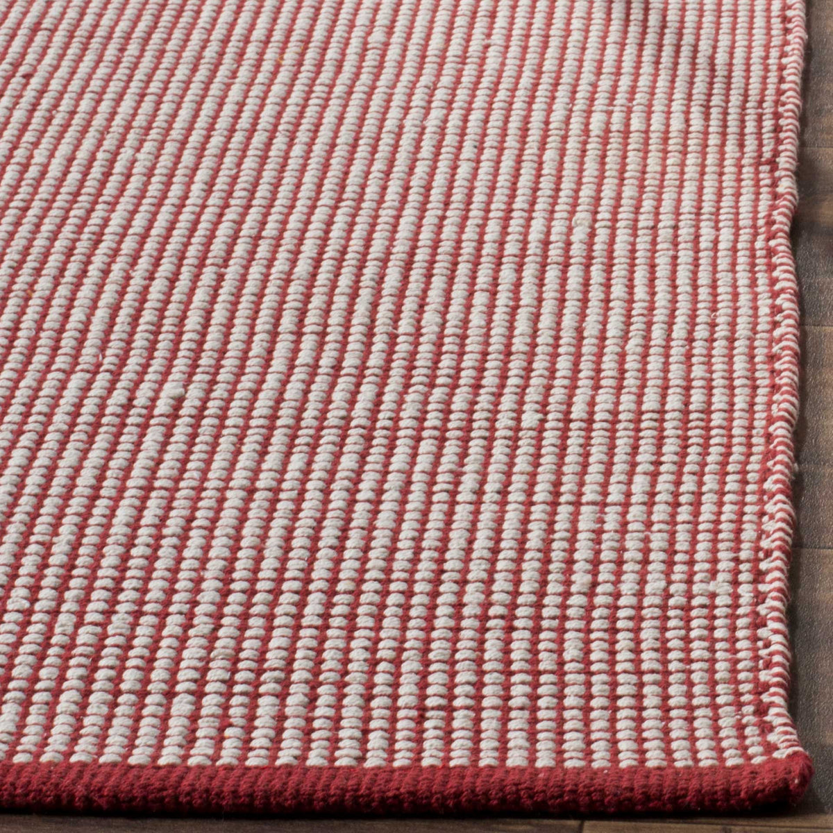 The vivid red bound edge frames raised ivory checks on a softly textured cotton rug.