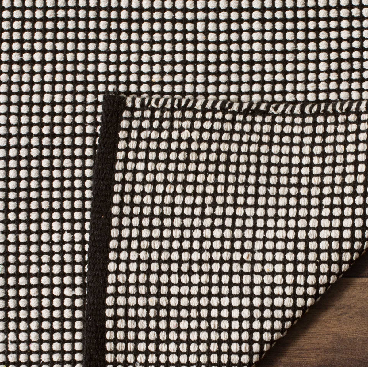 A folded edge exposes the dense ivory and black backing weave and its dark trim.