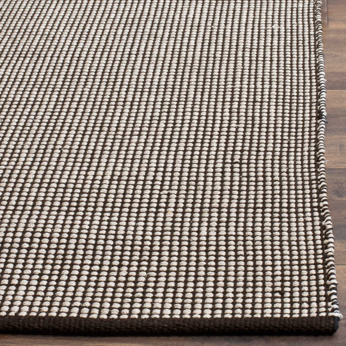 Small ivory cotton loops punctuate dark yarns and meet a neatly bound rug edge.