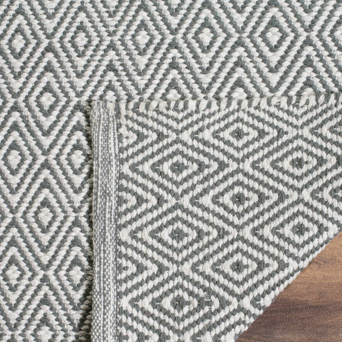 The folded corner shows the ivory and gray rug's woven underside and bound edge