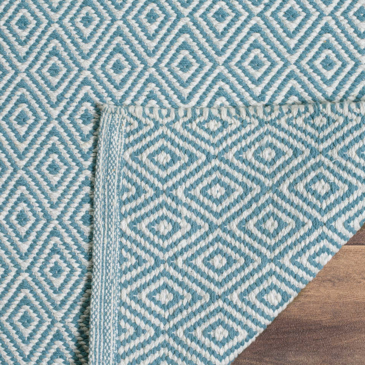 Lifting a corner reveals the woven underside and blue-trimmed edge of the ivory rug