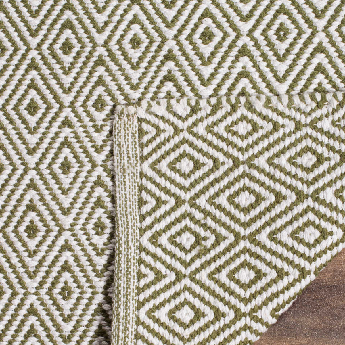 Folded edge reveals the woven reverse of a green and ivory diamond rug