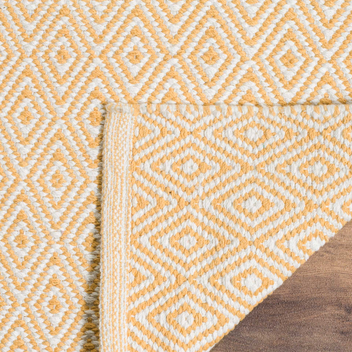A lifted corner reveals the ivory and gold rug's woven reverse and tidy border
