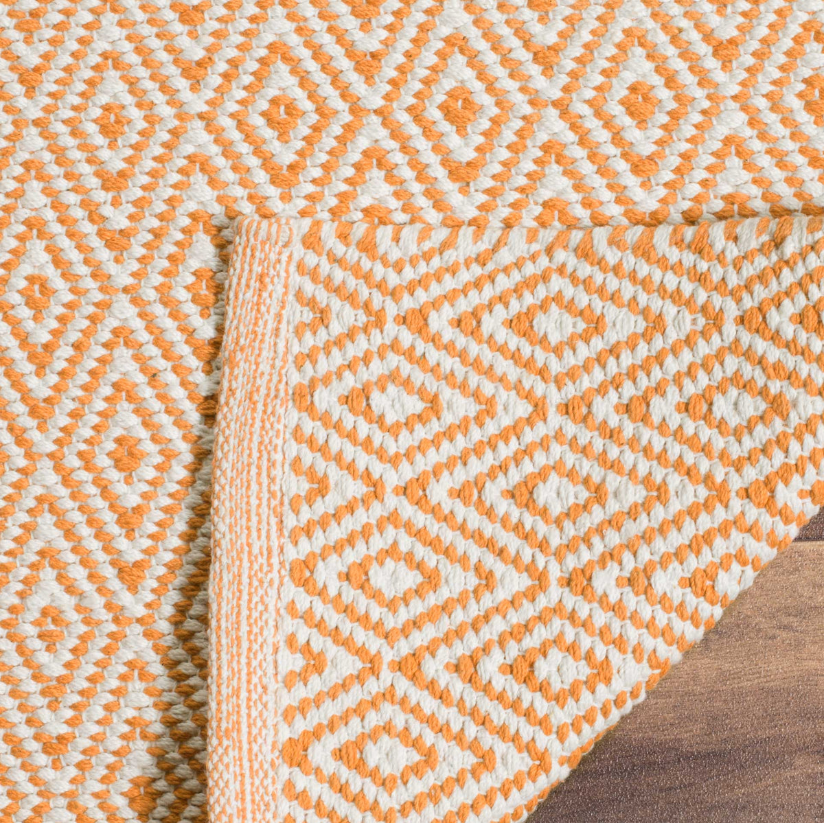 A folded corner reveals the rust and ivory rug's patterned woven reverse