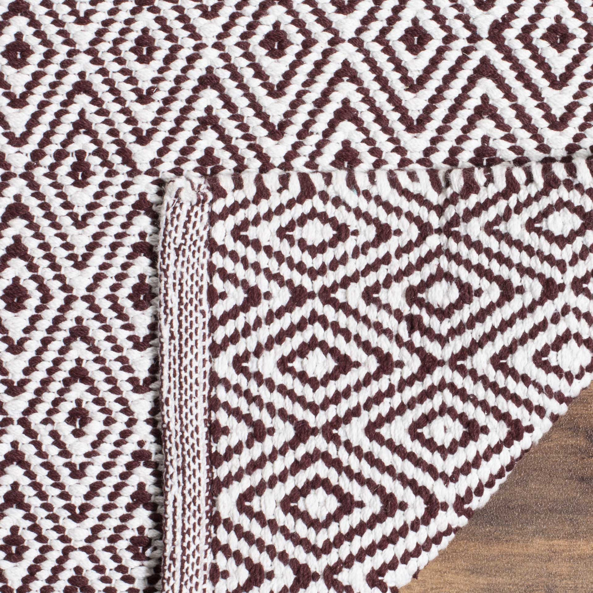A folded corner reveals the woven reverse of the chocolate and ivory geometric rug