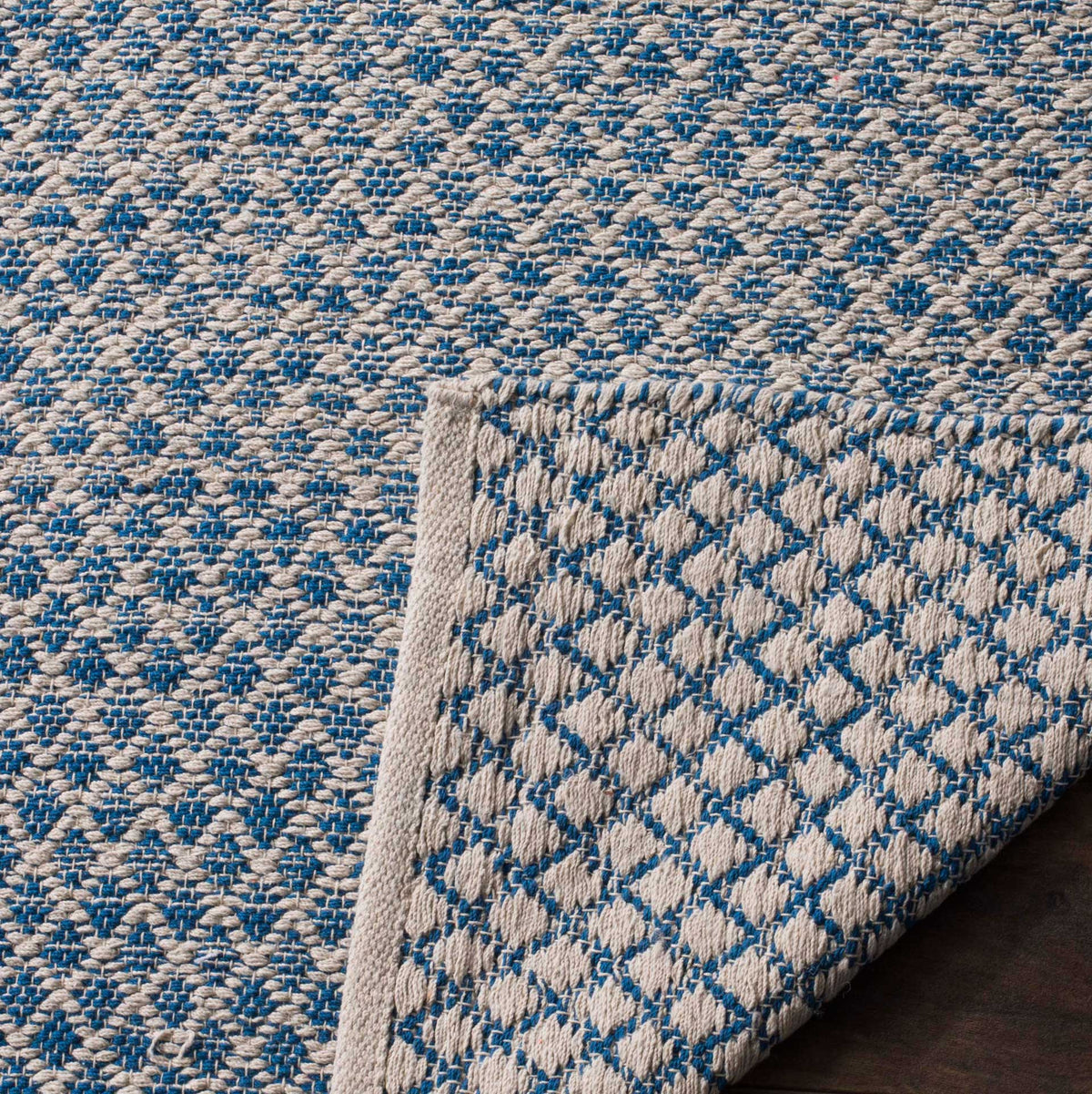 A lifted corner exposes the blue and ivory rug's woven underside and tidy bound edge.