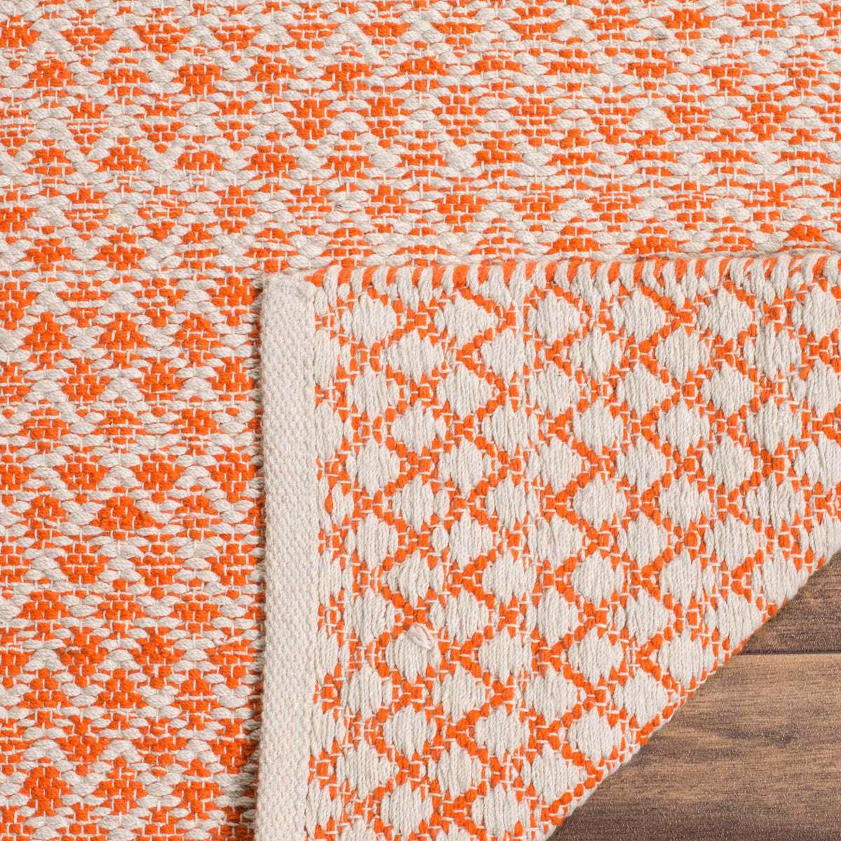 A turned corner reveals the orange and ivory woven underside and bound rug edge.