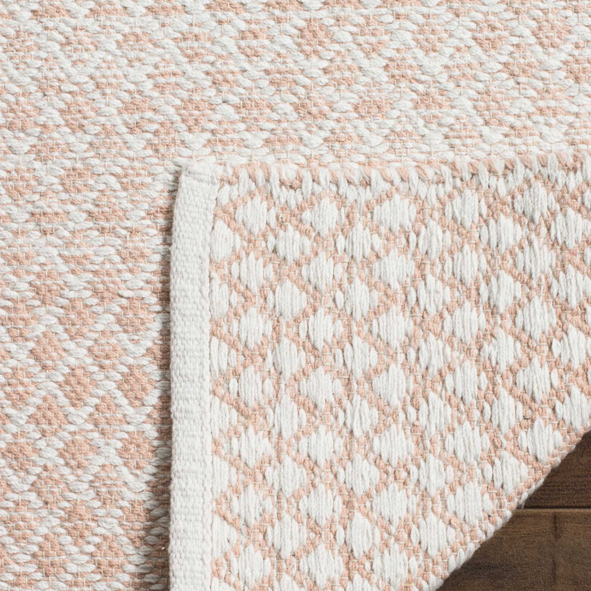 A folded corner reveals the beige and ivory rug's patterned underside and finished edge.