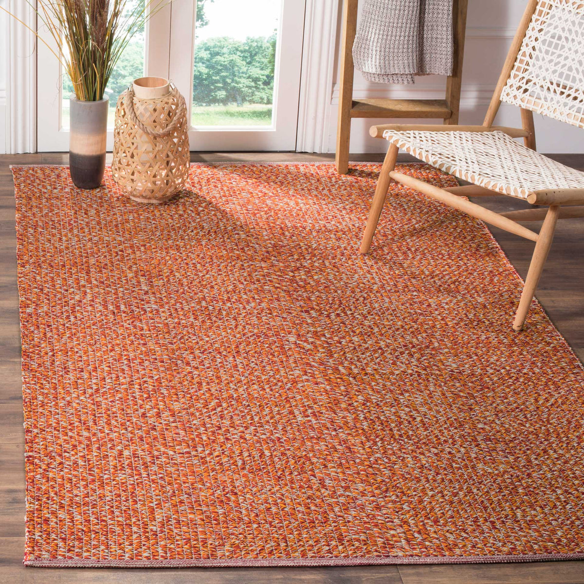 Orange woven area rug brightens the space beneath a natural wood lounge chair