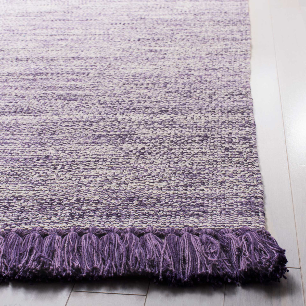 Plush purple tassels finish a delicately woven rug with soft tonal variation.