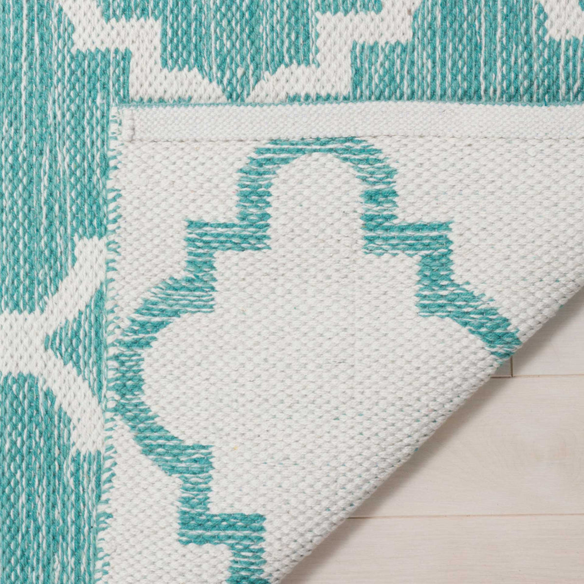 A folded corner reveals the ivory woven underside and teal pattern on the rug's reverse.