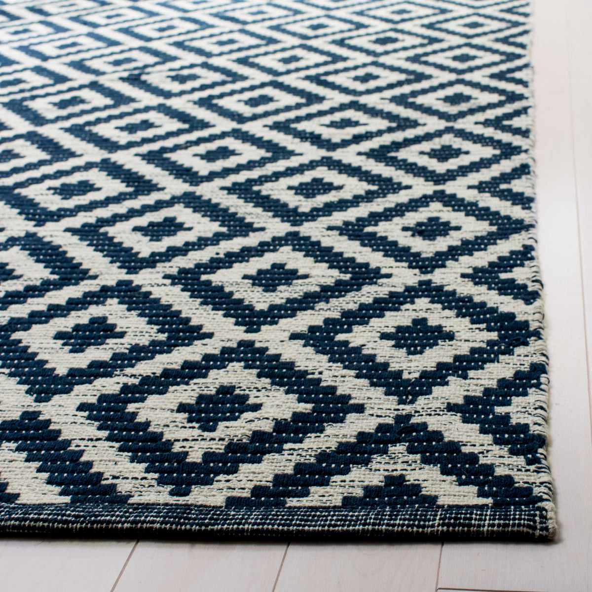 Textured navy diamonds and a narrow bound edge enrich the rug's ivory cotton weave.