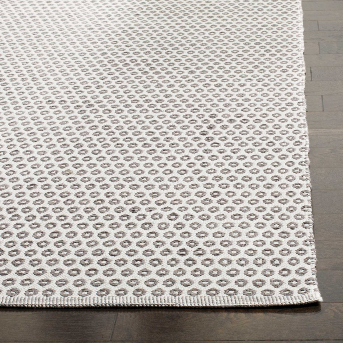 Neatly finished ivory rug edge frames tightly spaced gray rings and a textured cotton weave