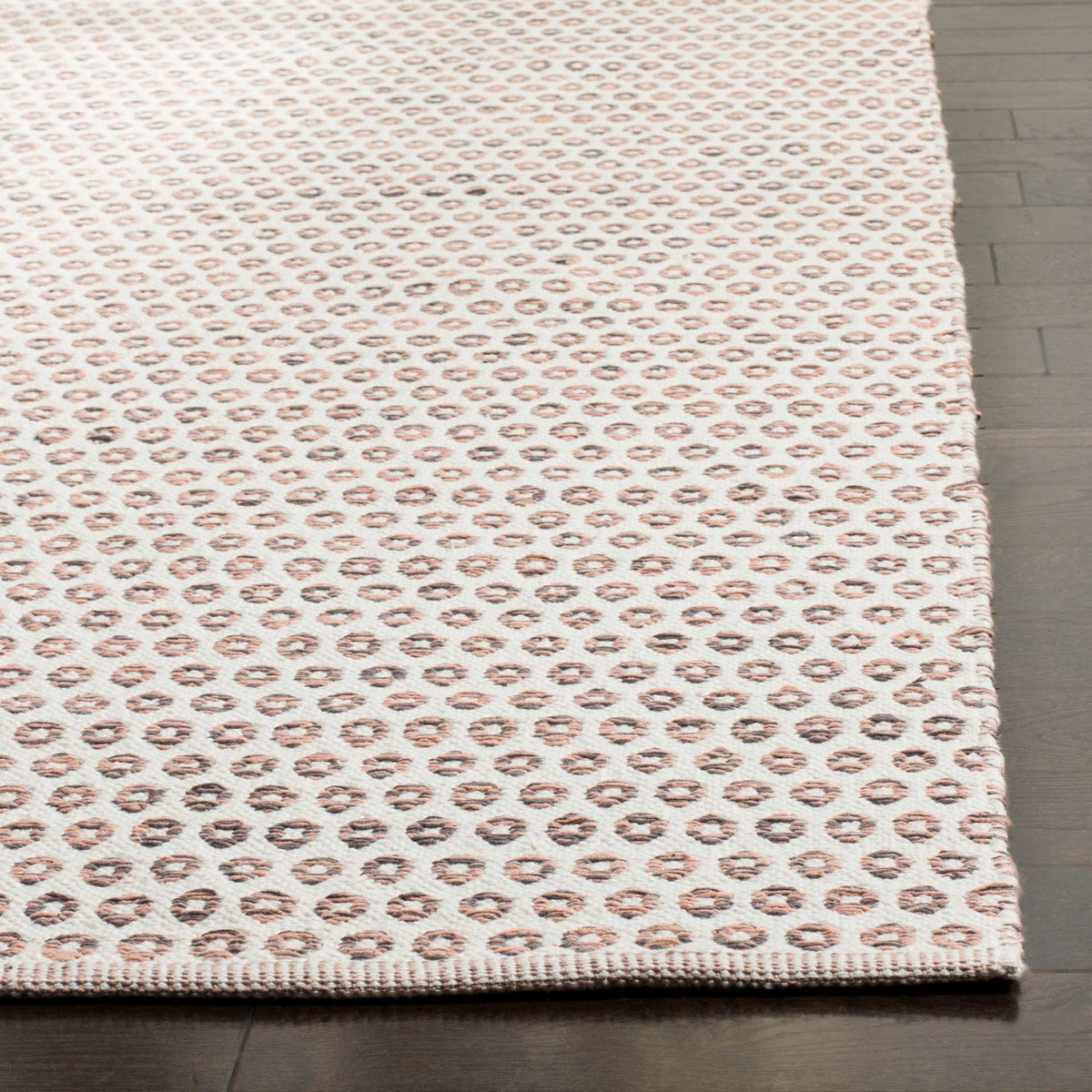 Peach and charcoal rings highlight the cotton texture and neatly finished edge of this ivory rug