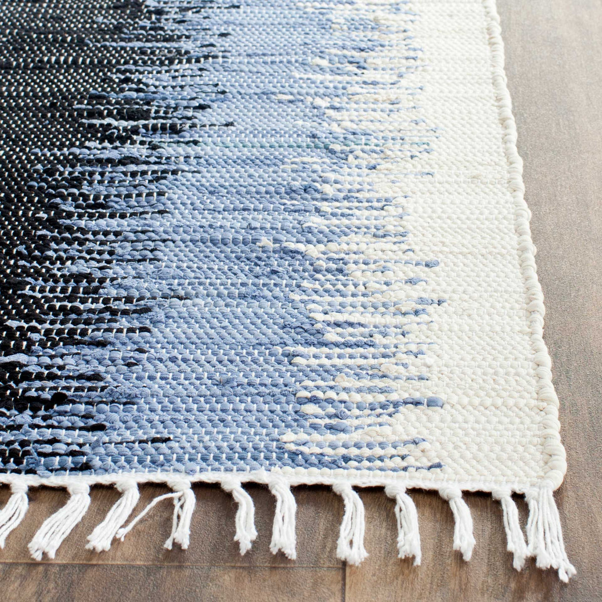 Textured cotton weave blends black, blue-gray, and ivory, finished with a bound edge and knotted fringe