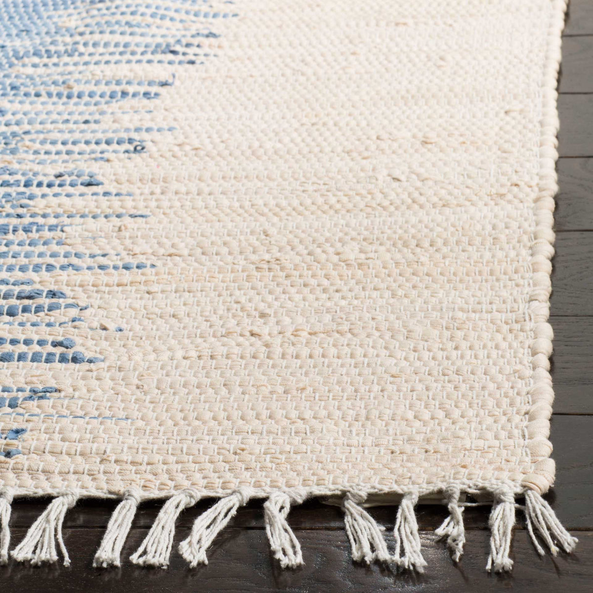 Knotted fringe and an ivory woven edge highlight the rug's textured cotton and blue accents.