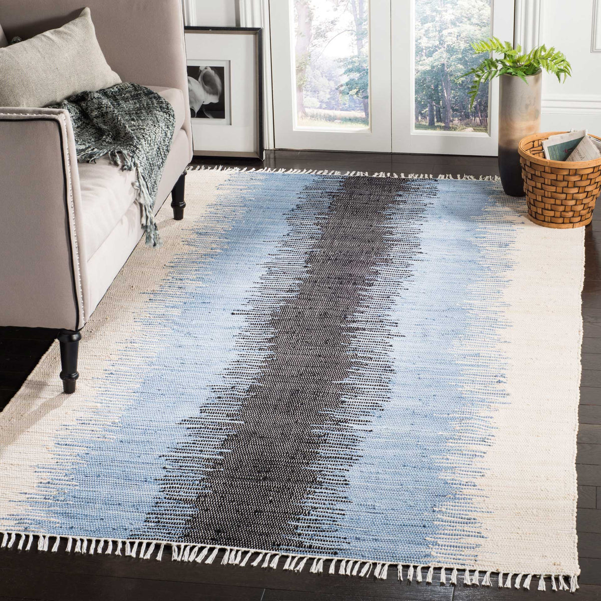A fringed rug with charcoal and blue brushstrokes anchors a sunlit living space.