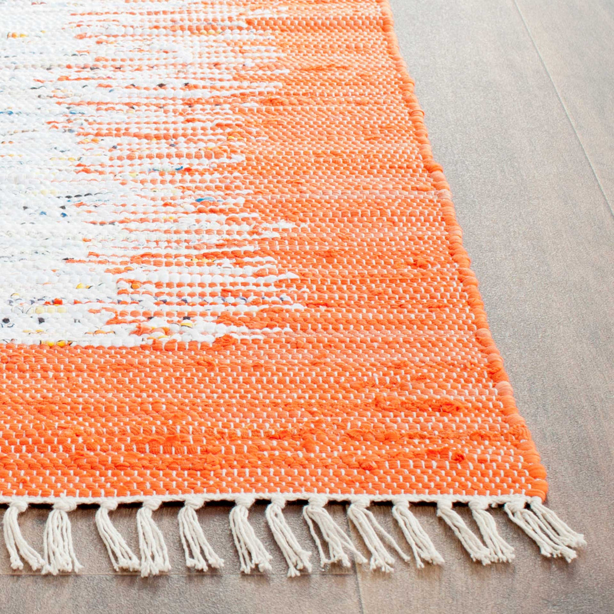 Orange woven threads mingle with ivory streaks and colorful flecks above a row of ivory fringe.