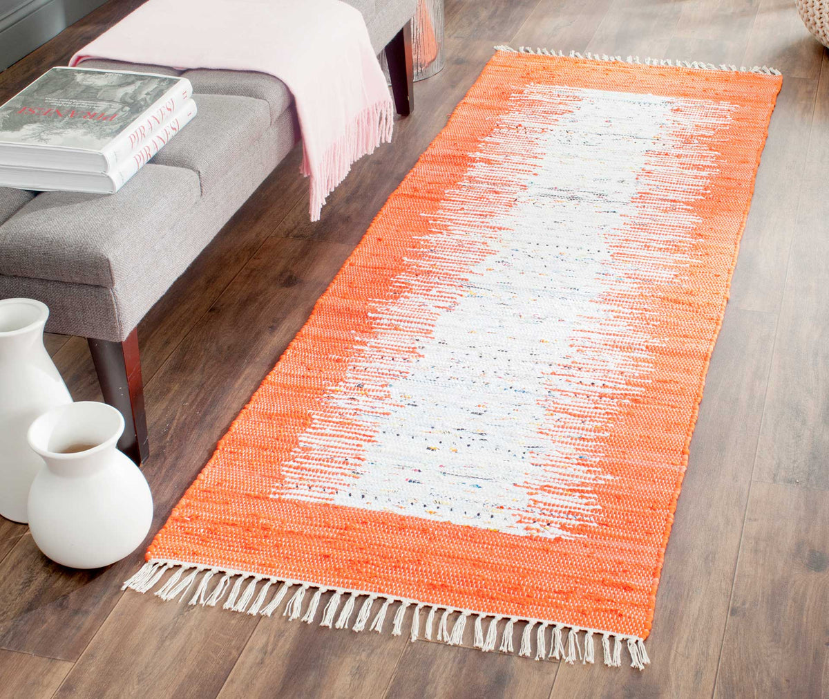 Vibrant orange frames the ivory runner, bringing cheerful color to a wood-floored living area.