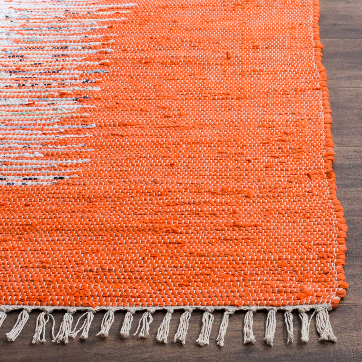 Cream fringe softens the corner of a bright orange handwoven cotton rug with flecks of ivory.
