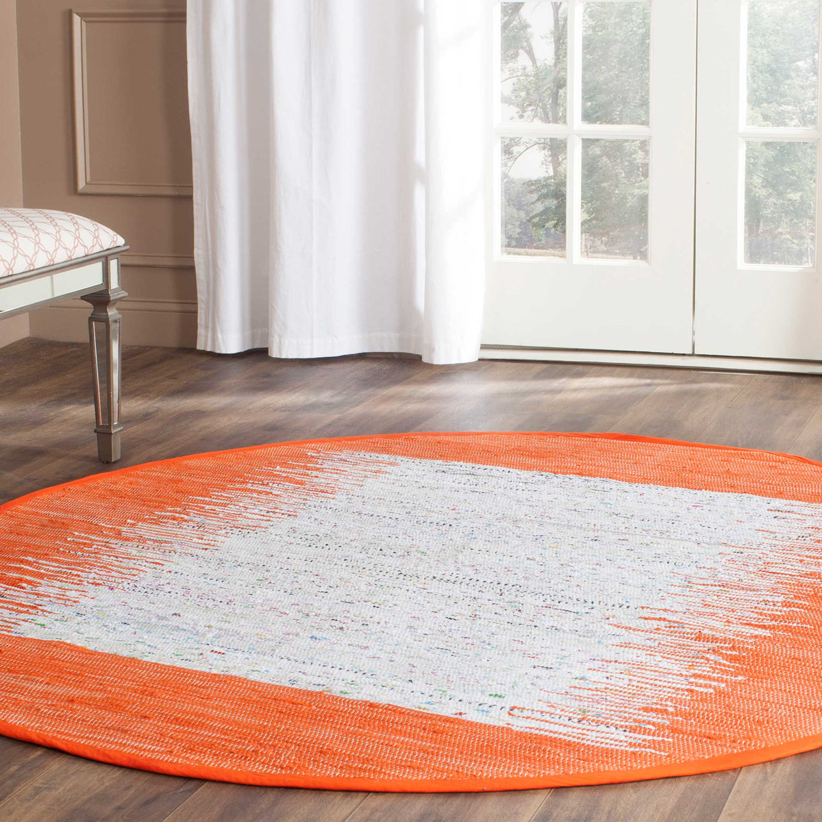A round ivory cotton rug stands out against wood flooring with its vibrant orange border